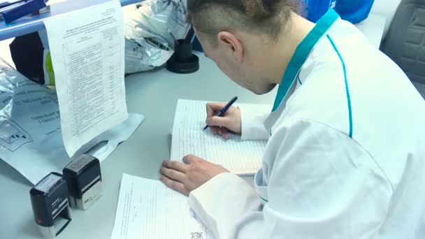 Człowiek w białym płaszczu pisze notatkę ręcznie w laboratorium — Wideo stockowe