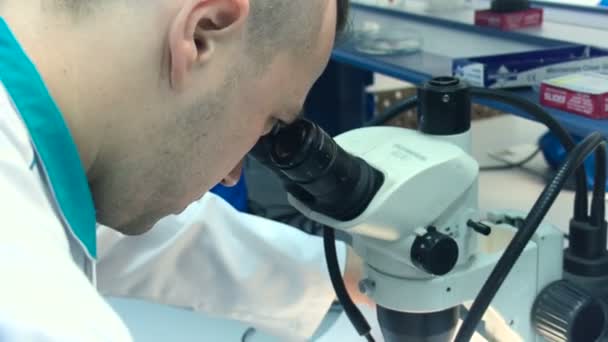 Un hombre con una capa blanca mirando en un microscopio en el primer plano del laboratorio — Vídeo de stock