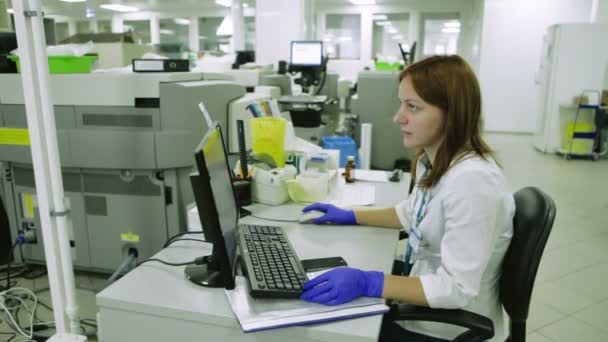 Młoda kobieta naukowiec w gumowe rękawice pracując na komputerze, przetwarzanie danych do badań w laboratorium medyczne. Połowie strzał — Wideo stockowe