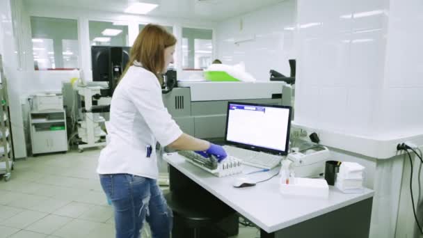 ゴム手袋で若い女性の科学者は、結果をコンピューターに入る。医療研究室でのサンプル チューブを引っ張る — ストック動画