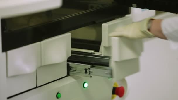 Young Female Scientist Loads a Tray With Test-Tubes Filled With Blood Into a Medical Machine. Hands in a Rubber Glowes — Stock Video