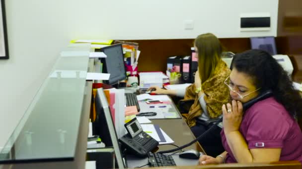 Due receptionist donne. Uno è responsabile per il telefono, le altre stampe sulla tastiera — Video Stock