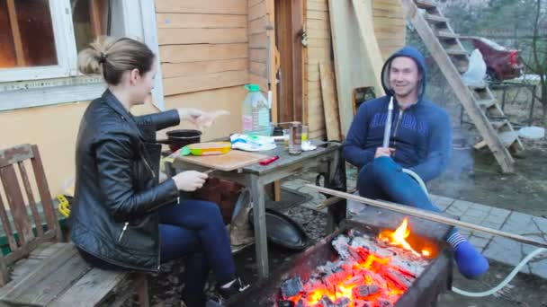 Mladý pár muž a žena na dovolené. Dívka nakrájíme maso na Barbecue, člověk směje a kouření vodní dýmky — Stock video