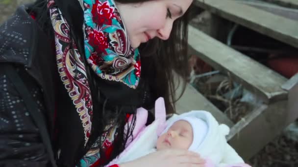 Jeune belle fille brune mère assise sur les marches de la pauvre maison en bois et tenant dans ses bras son nouveau-né fille. Plan rapproché — Video