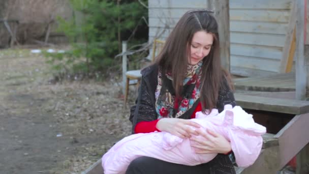 Giovane bella bruna ragazza madre seduta sui gradini della povera casa di legno e tenendo in braccio la sua neonata. Russia, Inverno, Freddo — Video Stock