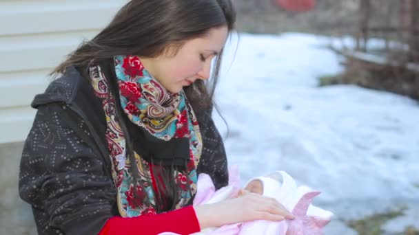 Giovane bella ragazza bruna madre vicino alla povera casa di legno che tiene tra le braccia la sua neonata. Primo piano. Russia, Inverno, Freddo, Neve, Amore — Video Stock