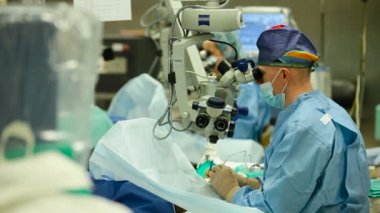 Göz hastalıkları. Erkek doktor kuralları göz ameliyatı istimal mikroskop ve bir hemşire ile ona yardımcı olur. Görme restorasyon. Katarakt kaldırma, vitreus