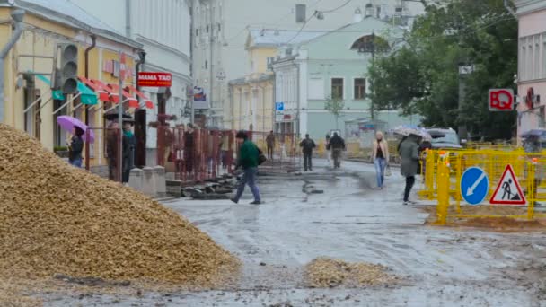 Folk går ned ad gaden med paraplyer. Regnvejrsdag i byen. Reparationer på gaden – Stock-video