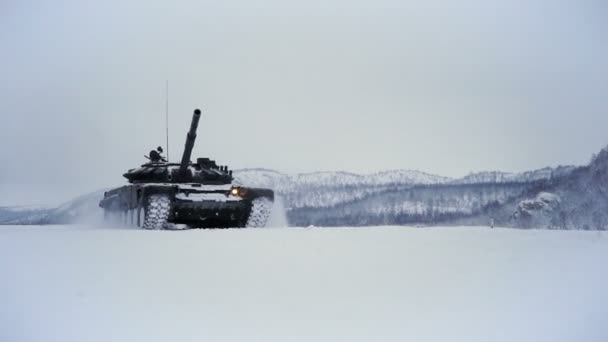 Заснеженное поле стрельбища на фоне горы. Протаранивший танк едет по полю — стоковое видео