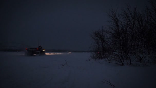 Champ de polygones enneigés dans les hautes terres. Le véhicule blindé de transport de troupes roule sur le terrain la nuit — Video