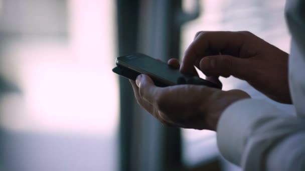 El hombre usa el teléfono. El hombre está junto a la ventana en el interior. Vista de cerca — Vídeo de stock