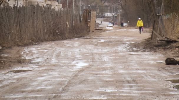 スラッシュと泥で湾曲した道路。黄色のジャケットの女性が歩いている — ストック動画