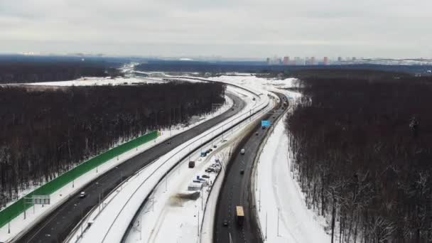 Большое шоссе в лесу зимой. Город вдалеке. Движение транспорта — стоковое видео