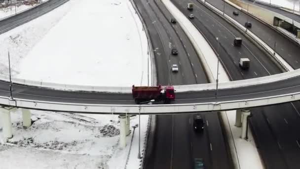 Вид на большое шоссе в лесу зимой. Город вдалеке. Красный грузовик едет по развязке. — стоковое видео