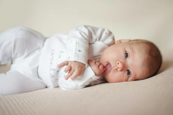 Bebé está acostado sobre cuadros brillantes en pijama blanco —  Fotos de Stock