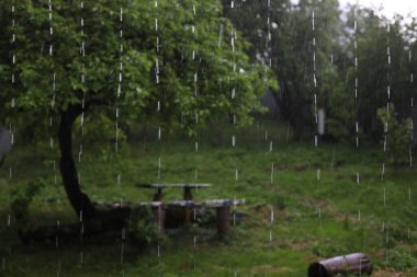 Yağmurlu, bulutlu bir gün. Yağmur damlaları ve arka plandaki ağacın altında bir masa..