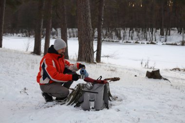 Turuncu ceketli bir adam kış ormanındaki teneke bardağa termostan çay döker..