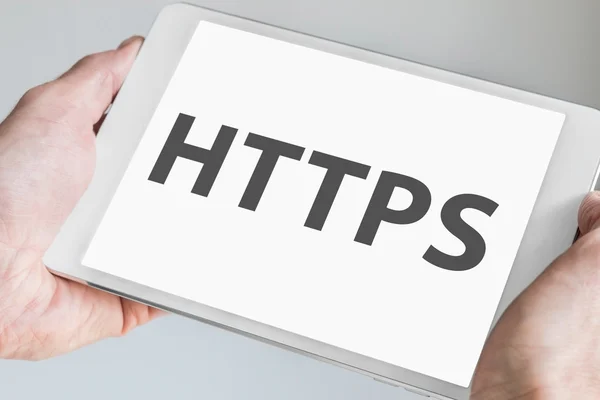 HTTPS text displayed on touch screen of a modern tablet. Hands holding mobile device to browse the internet — Stockfoto