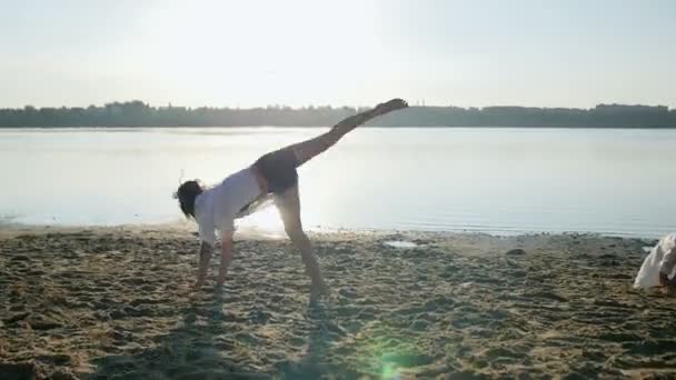 Flickan gör gymnastiska knäppa på sandstrand nära lake — Stockvideo