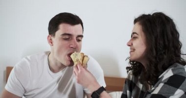Mutlu bir erkek ve kadın evde bir yatakta pizza yiyorlar. Mutlu genç aşıklar birlikte vakit geçirmekten zevk alırlar.