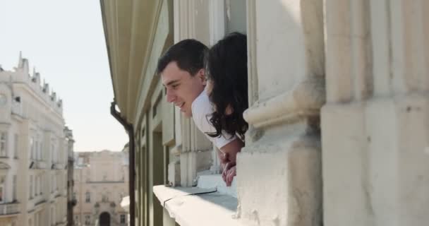 Ein junges Paar sitzt auf dem Fensterbrett und genießt den Blick auf die Altstadt. Glückliche junge Verliebte genießen die gemeinsame Zeit zu Hause — Stockvideo