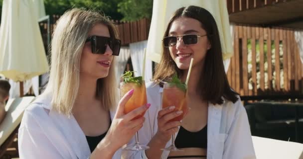 Két nő szexi fürdőruhában lazít a medence közelében. Utazás és nyaralás a luxus szállodában. Két lány alkoholos italokkal szórakozik együtt nyaralóhelyen.