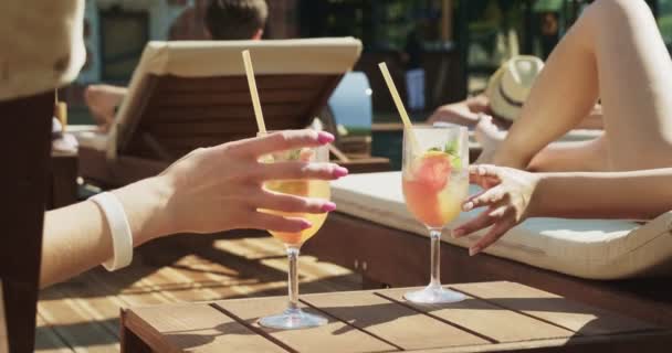 Deux femmes en maillots de bain sexy se détendent près de la piscine. Voyager et passer des vacances dans un hôtel de luxe. Deux filles avec des boissons alcoolisées s'amusent ensemble sur la station de vacances Séquence Vidéo Libre De Droits