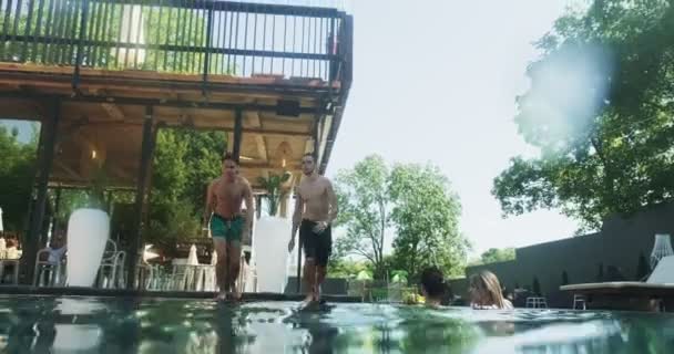 Vänner hoppar i poolen under vattnet och har kul att fira sommarsemester tillsammans. Grupp av unga män njuta av pool fest Royaltyfri Stockvideo