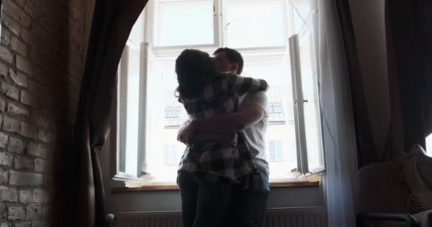 Fiatal pár férfi és nő maradjanak otthon az ablak közelében. Boldog fiatal szerelmesek élvezik az együtt töltött időt otthon. Stock Videó