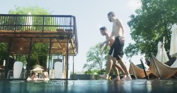 Vänner hoppar i poolen under vattnet och har kul att fira sommarsemester tillsammans. Grupp av unga män njuta av pool fest Videoklipp