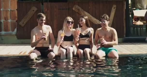 Un grup de prieteni se distrează la piscină. Oamenii beau cocktail-uri de vară la un hotel de lux în vacanță tropicală. Ochelari de petrecere însorită cu cocktail-uri de fructe lângă piscină Secvență video de stoc fără drepturi de autor