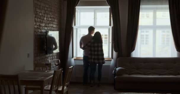 一对年轻夫妇呆在家里靠窗的地方.快乐的年轻夫妇喜欢在家里共度时光 图库视频片段