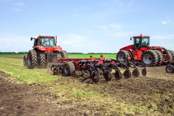 Ein moderner, roter Traktor pflügt im Frühjahr auf einem grünen Acker auf dem Hof. Erntemaschine sät Weizen. — Stockfoto