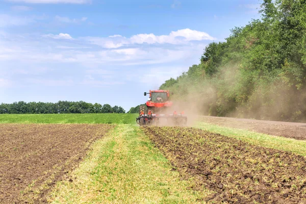 Tractor rojo de tecnología moderna arando un campo agrícola verde en primavera en la granja. Cosechadora siembra trigo. — Foto de Stock