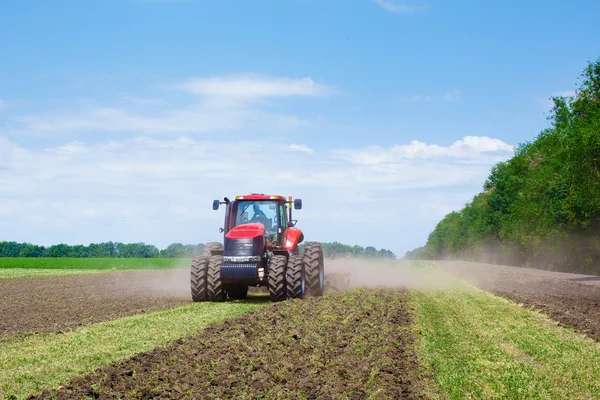 Modern teknoloji kırmızı traktör ilkbaharda çiftlikte yeşil tarla sürüyor. Buğday eken hasatçı.. — Stok fotoğraf