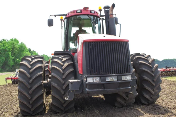 Современный технический красный трактор вспахивает зеленое сельскохозяйственное поле весной на ферме. Урожай пшеницы. — стоковое фото