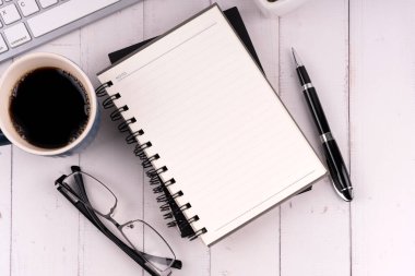 Bir fincan kahve ve bilgisayar klavyeli boş not defteri.