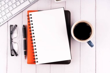 Bir fincan kahve ve bilgisayar klavyeli boş not defteri.