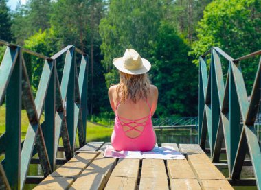 Göl kenarında oturan mayolu sarışın bir kadının arka görüntüsü.