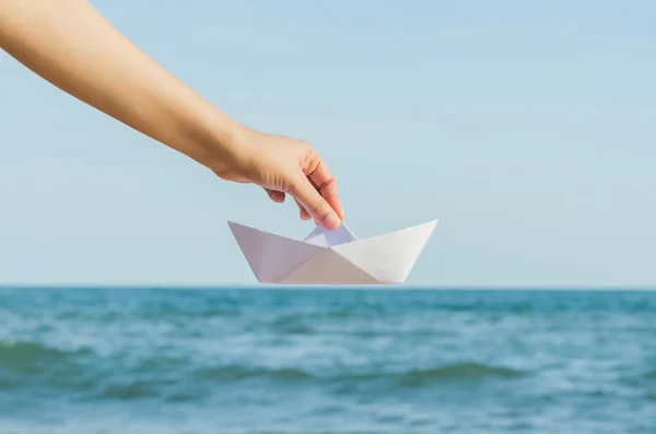 Kvinnliga handen håller papper båt på havet bakgrunden — Stockfoto