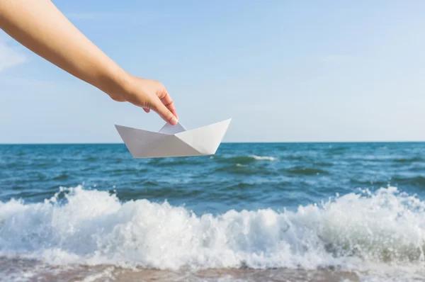 Mão feminina segurando barco de papel no fundo do mar — Fotografia de Stock
