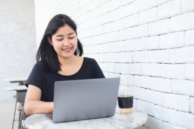 Genç Asyalı kadın, kafede dizüstü bilgisayarla çalışıyor. İş kadını daktilo ediyor, modern kafede arama yapıyor. Çevrimiçi teknoloji sistemi kavramı çalışıyor.
