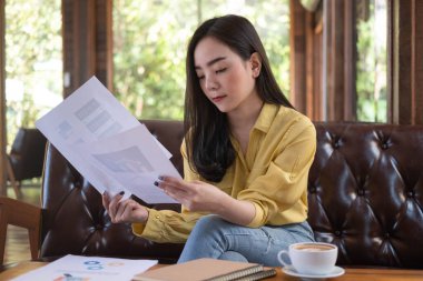 Genç Asyalı iş kadını kafede oturuyor ve dokümanları okuyor. Toplantıdan önce mali belgeler ve mali raporlarla çalışan kadın. 