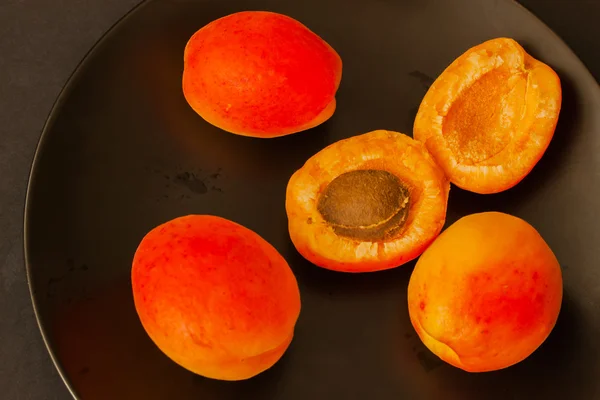 Ripe apricots in dark plate on black background