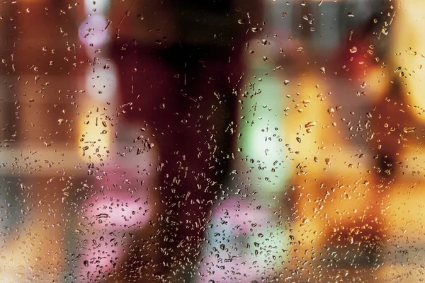 Ventana húmeda con gotas de lluvia, calle borrosa bokeh. Resumen borroso fondo colorido. Concepto de tiempo, estaciones, ciudad por la noche — Foto de Stock