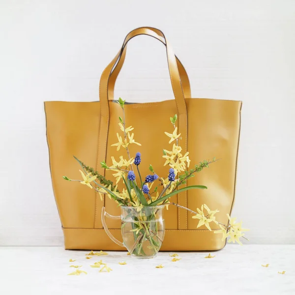 Жовта сумочка і букет з диких квітів у вазі на світлому фоні. Концепція сезонних весняних або літніх покупок — стокове фото
