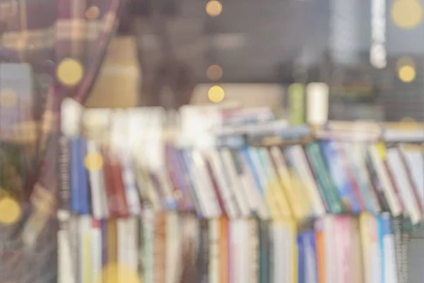 Homályos könyvespolcok színes könyvespolcokkal az üzlet ablaka mögött. Könyvek olvasása és értékesítése. — Stock Fotó