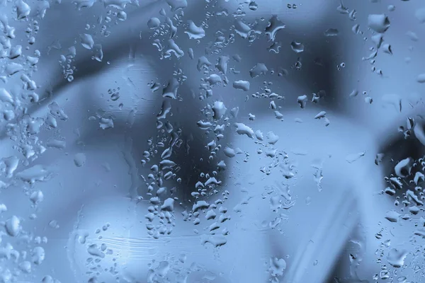 Abstract background with raindrops on wet glass. Blurred style, selective focus, soft blue grey color