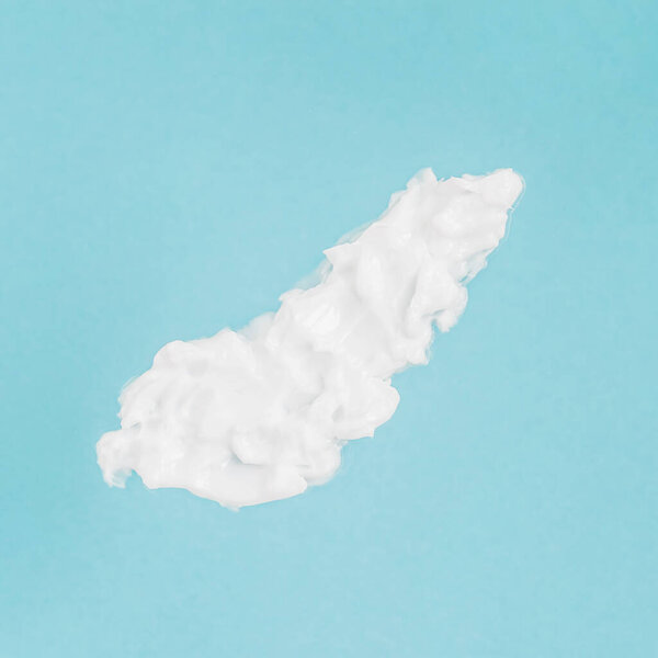 Мазок косметического крема для лица и тела. Белая текстура на синем фоне