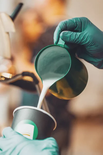 Close-up de mãos barista derramando leite quente com espuma de jarro em copo de papel, preparação de cappuccino café — Fotografia de Stock